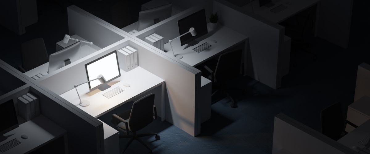 view of a dark office containing empty cubicles with lighting on only one cubicle