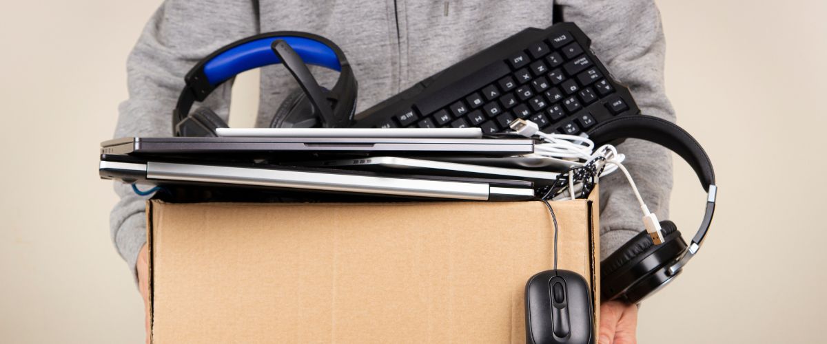 person holding a box containing laptops, tablets, keyboards, headphones and computer mouse